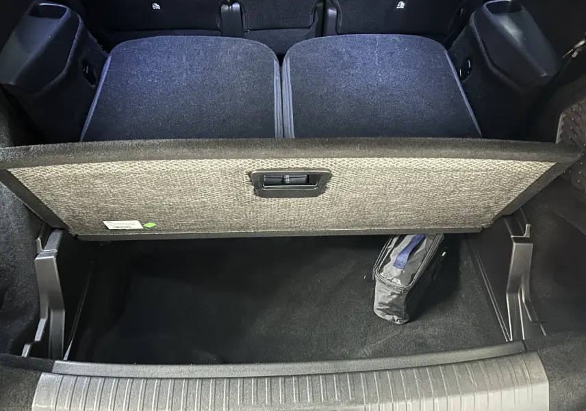 Vue plongeante sur le coffre ouvert du Peugeot 5008 gris Artense, montrant la tablette de séparation et un sac de rangement noir.