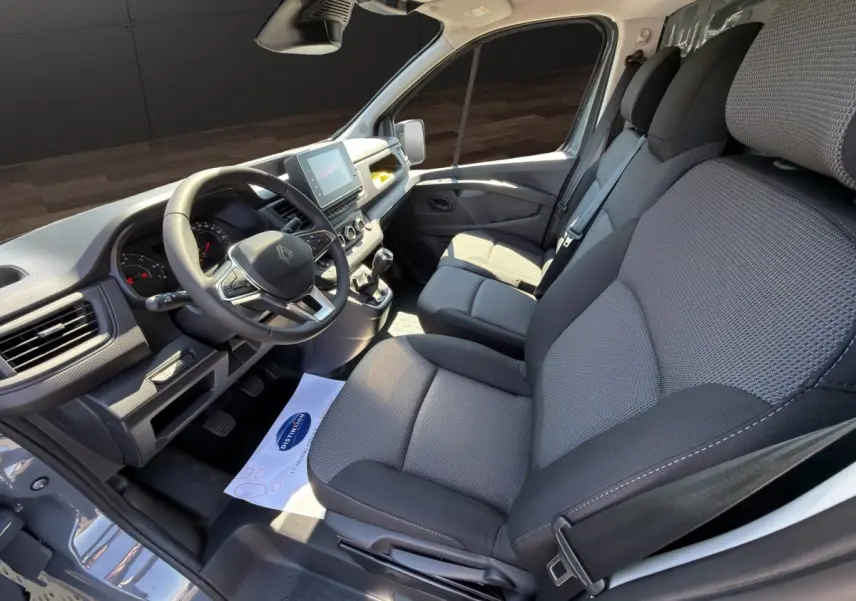 Vue intérieure côté conducteur du Renault Trafic Fourgon gris foncé, montrant le volant multifonctions et les sièges tissu gris.