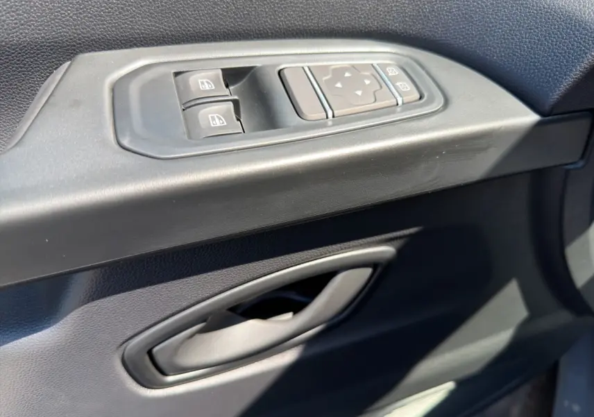 Gros plan sur la commande des vitres électriques et réglage des rétroviseurs côté conducteur du Renault Trafic Fourgon gris foncé.