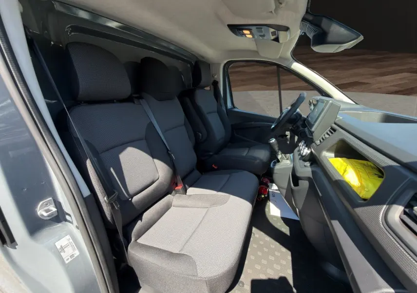 Intérieur du Renault Trafic Fourgon gris foncé, vue côté conducteur montrant les sièges avant et le tableau de bord.