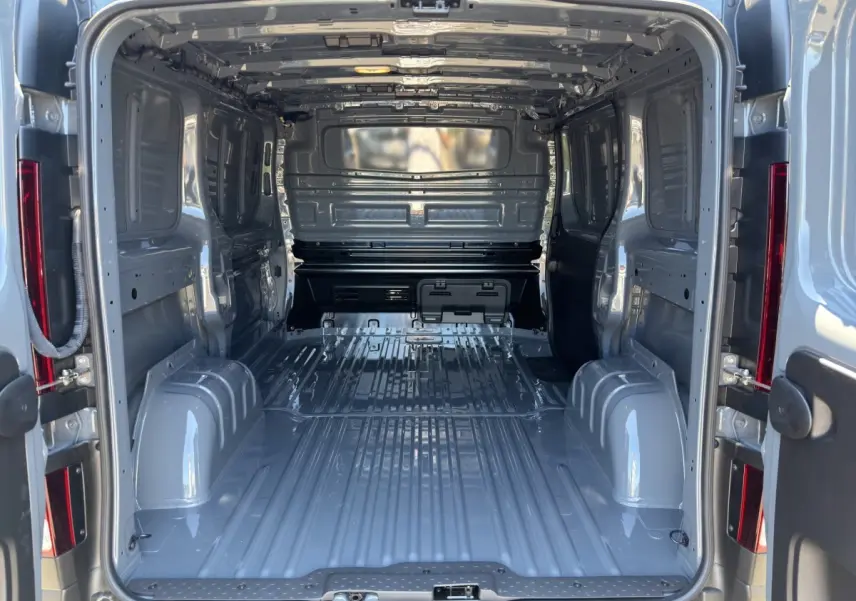 Vue intérieure arrière du fourgon Renault Trafic L1H1 gris foncé, montrant l'espace de chargement vide et la cloison pleine.