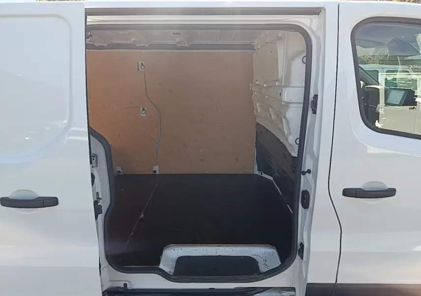 Vue latérale droite sur l’ouverture de la porte coulissante d’un Renault Trafic Fourgon blanc, montrant l’espace de chargement vide.