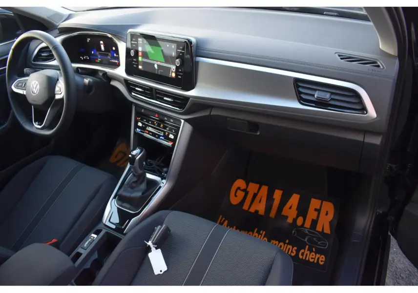 Vue intérieure côté passager avant du Volkswagen T-Roc 2025, sellerie tissu noir et console centrale moderne.