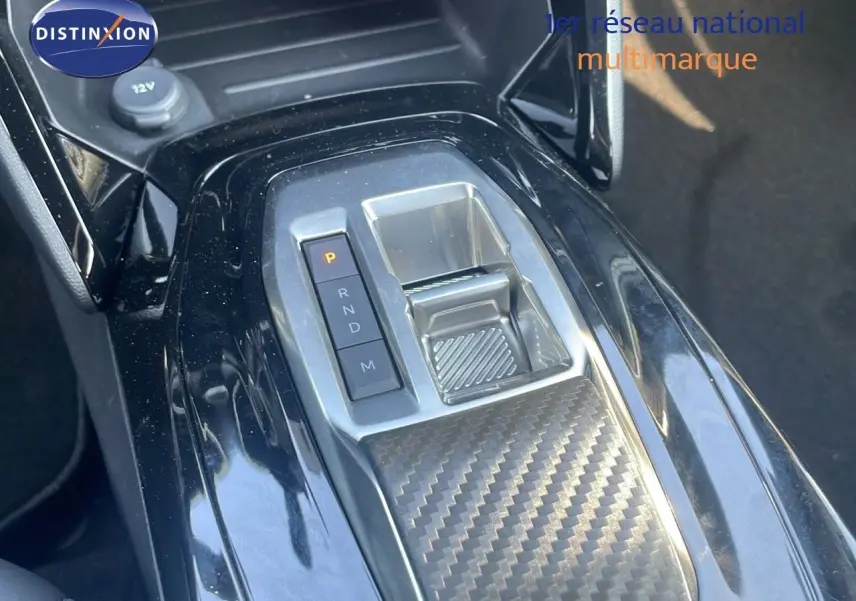 Gros plan sur la console centrale de la Peugeot 2008 Hybrid 136ch Allure 2025, avec levier de vitesses automatique et finition carbone.