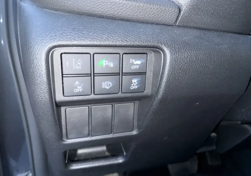 Gros plan sur les commandes noires du tableau de bord côté gauche du Honda CR-V Hybrid gris 2019, avec boutons d'assistance activés.