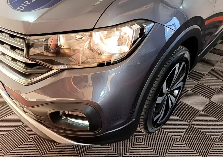 Gros plan sur l'avant droit du Volkswagen T-Cross gris foncé, mettant en valeur le phare allumé et la roue.