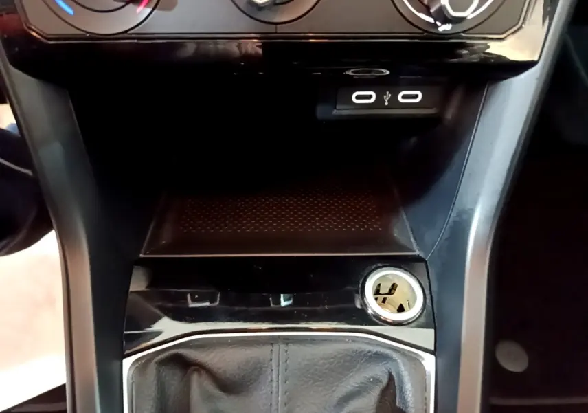 Vue rapprochée de la console centrale noire du Volkswagen T-Cross avec prises USB et allume-cigare visible.