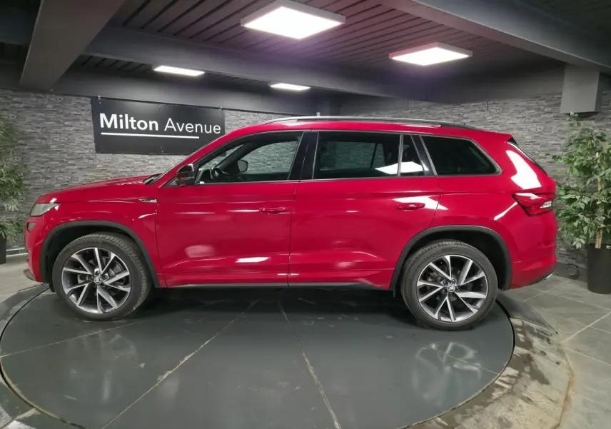 Vue latérale gauche d'un Skoda Kodiaq Sportline rouge métallisé avec jantes alliage 20 pouces dans un showroom intérieur.