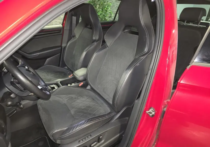 Vue intérieure côté conducteur d'un Skoda Kodiaq rouge 2021, sièges sport cuir/Alcantara noirs avec surpiqûres blanches.