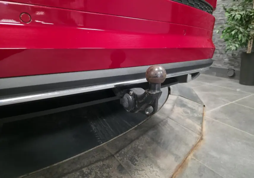 Gros plan sur le crochet d'attelage à l'arrière d'un Skoda Kodiaq rouge, avec pare-chocs et capteurs de stationnement visibles.