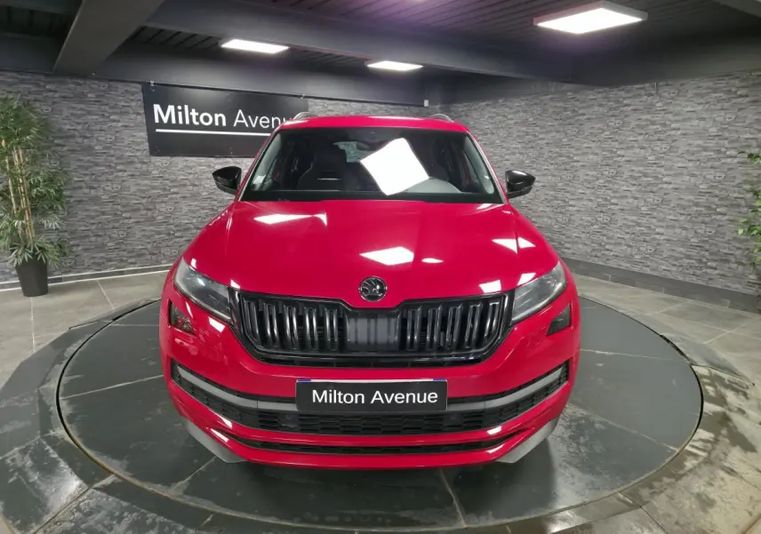 Vue avant d'un Skoda Kodiaq rouge 2021 avec calandre noire et plaque "Milton Avenue" en intérieur showroom.