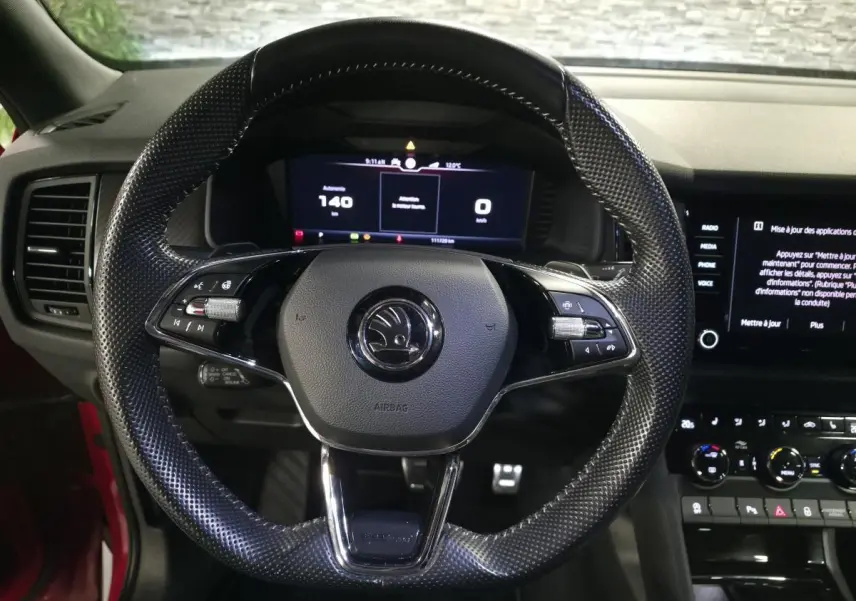 Vue intérieure centrée sur le volant cuir perforé noir du Skoda Kodiaq rouge, avec tableau de bord digital et écran tactile.