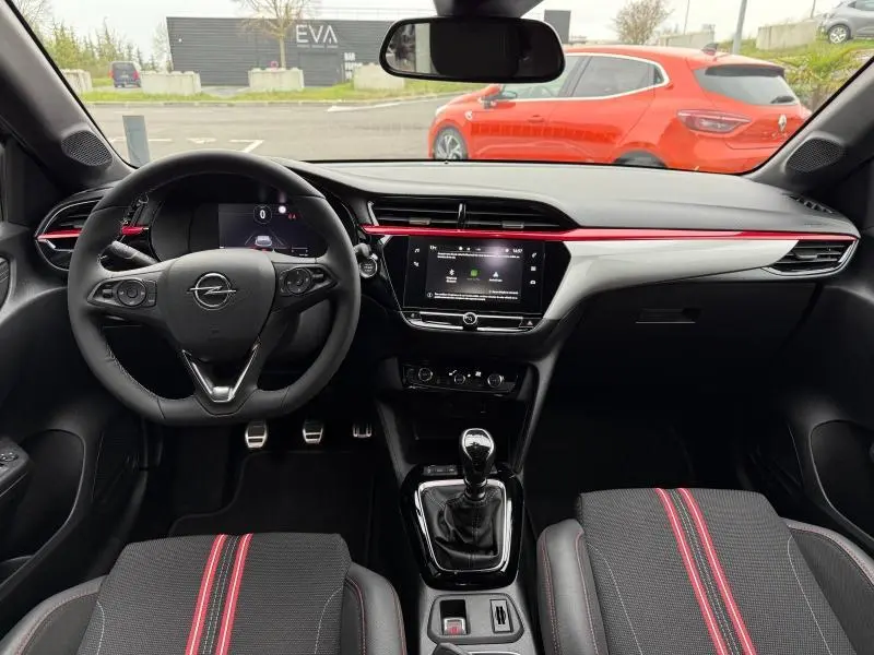 Vue intérieure avant de l’Opel Corsa 1.2 Turbo 2023, volant cuir, console centrale avec boîte manuelle et sièges noirs à bandes rouges.