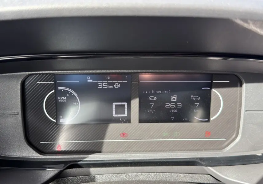 Gros plan sur le combiné d'instruments numérique du Citroën Berlingo blanc, affichant vitesse et consommation.