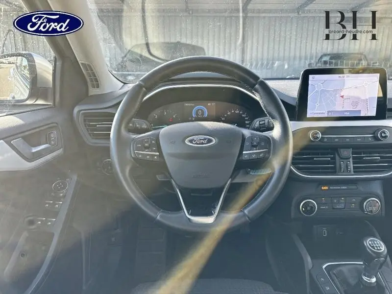 Vue intérieure du poste de conduite d'une Ford Focus 2020, volant cuir multifonction et écran tactile GPS visible.