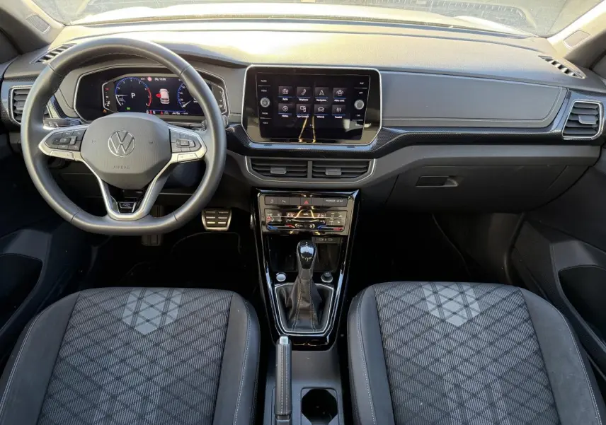 Vue intérieure avant du Volkswagen T-Cross 2025, tableau de bord noir avec écran tactile et sièges tissu à motifs géométriques.