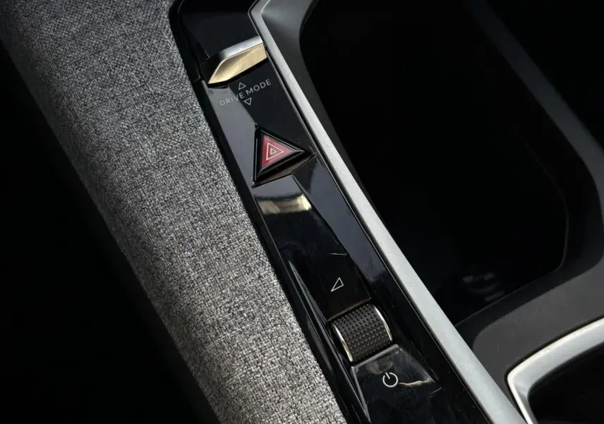 Gros plan sur la console centrale intérieure avec commandes Drive Mode et bouton warning, tissu gris et finitions noires brillantes.