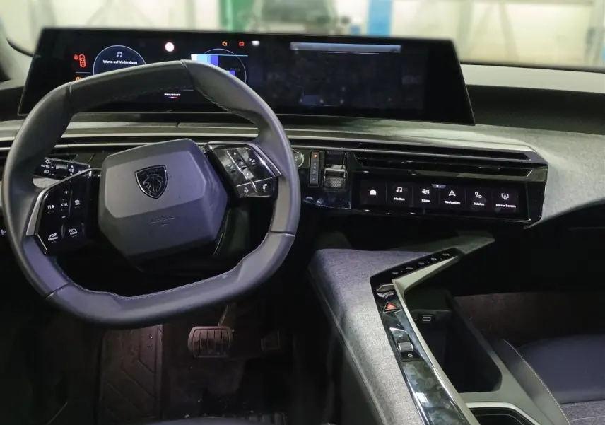 Vue intérieure du poste de conduite du Peugeot 3008 Hybrid 2025 avec volant compact cuir noir et écran panoramique incurvé.