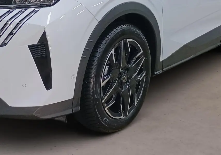 Gros plan sur la roue avant droite et l'aile blanche du Peugeot 3008 Hybrid 145 e-DSC6 Allure avec jante alliage noire et argent.