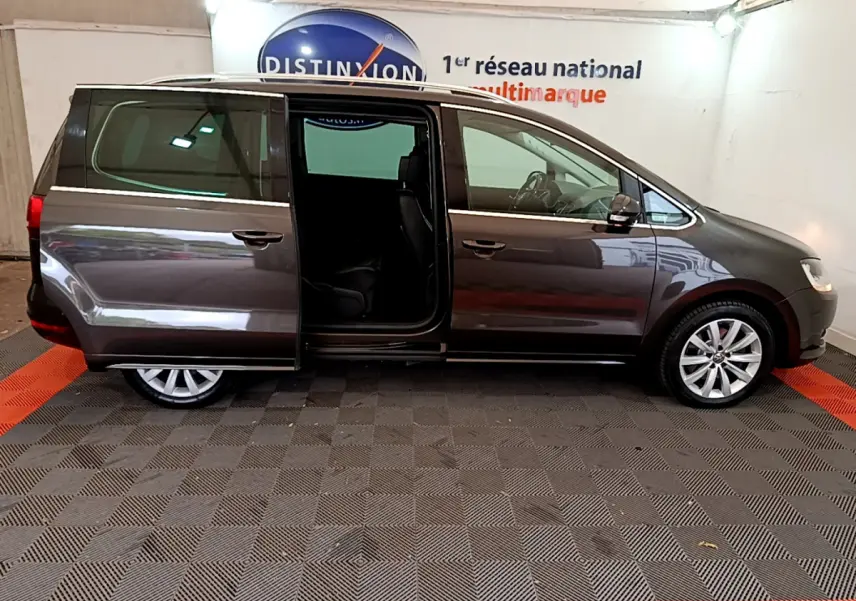 Vue latérale droite d’un Volkswagen Sharan marron 2017 avec porte coulissante arrière ouverte en intérieur showroom.