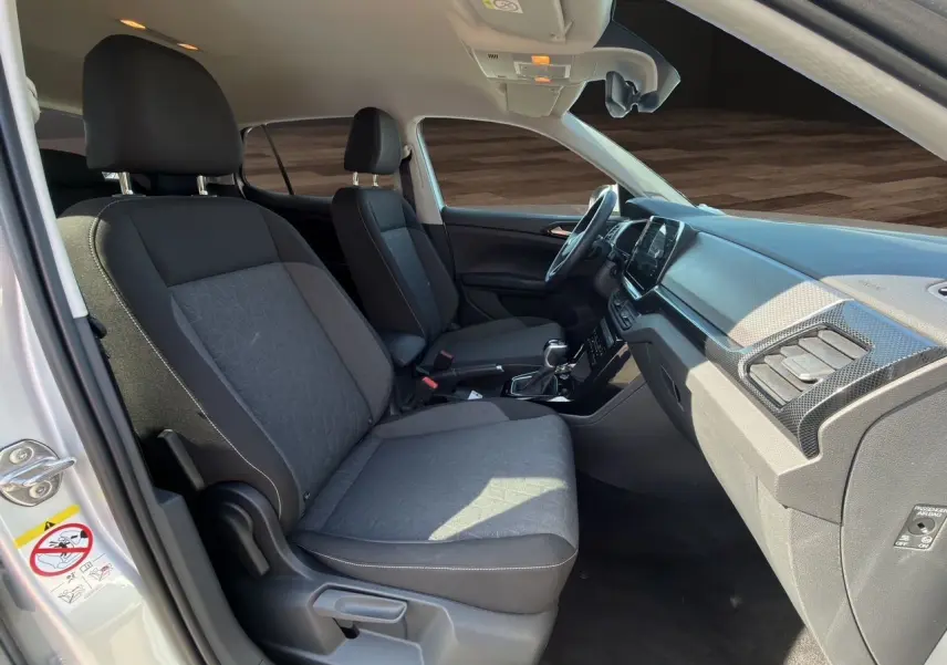 Vue intérieure côté conducteur du Volkswagen T-Cross 2025 argent, sièges tissu noir et tableau de bord moderne.