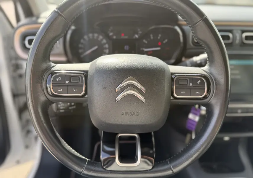 Vue rapprochée du volant noir de la Citroën C3 1.2 PureTech 83 Origins avec commandes intégrées et logo chromé central.