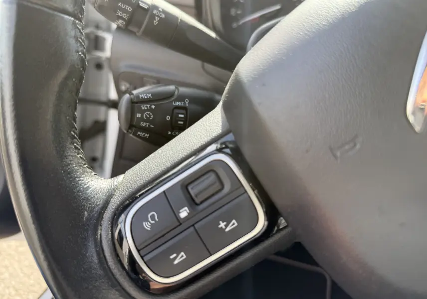 Gros plan sur le volant côté gauche de la Citroën C3 blanc toit noir, avec commandes audio et régulateur de vitesse visibles.