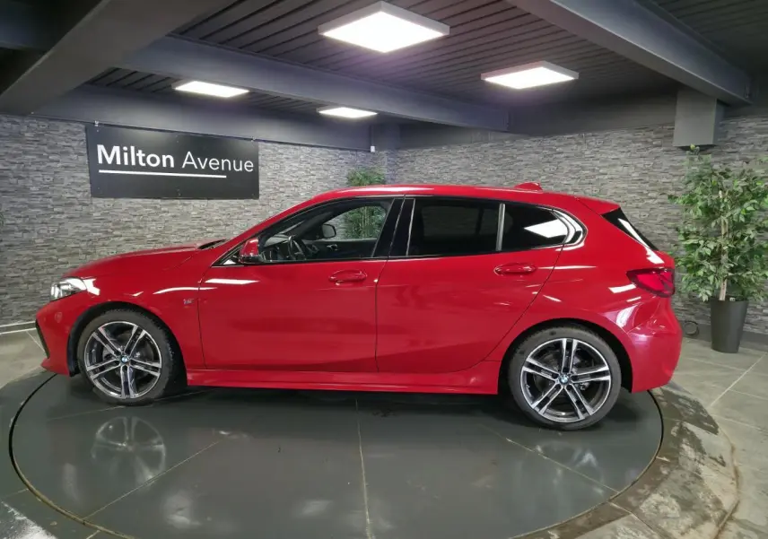 BMW Série 1 116d M Sport rouge vue de profil côté gauche, avec jantes alliage 18 pouces et badge M sur l'aile avant.
