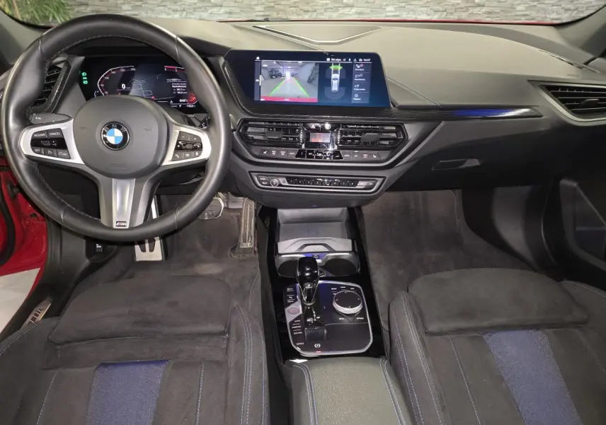 Vue intérieure avant de la BMW Série 1 116d M Sport 2024, sellerie tissu Alcantara noire avec inserts bleus et écran tactile central.