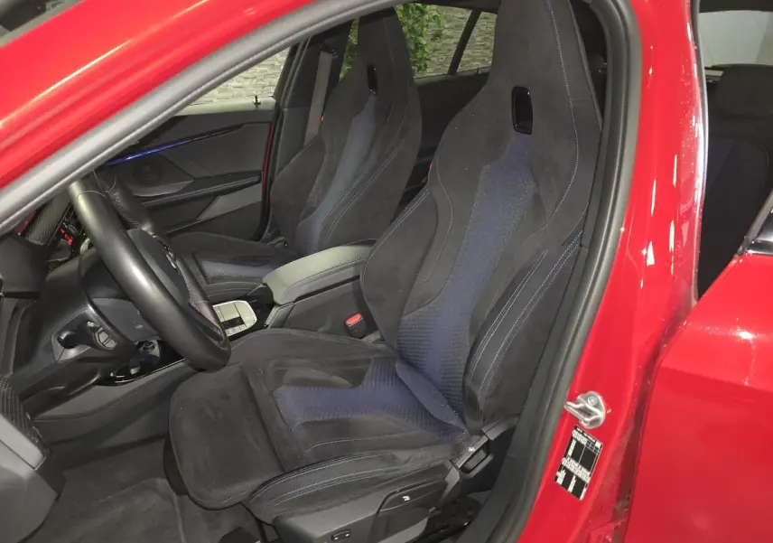 Vue intérieure côté conducteur d'une BMW Série 1 116d rouge avec sièges sport M en tissu et Alcantara noir.