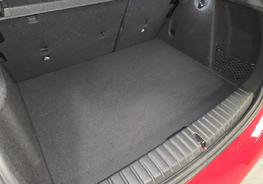 Vue rapprochée du coffre ouvert d'une BMW Série 1 116d M Sport rouge, montrant le tapis et les fixations internes.