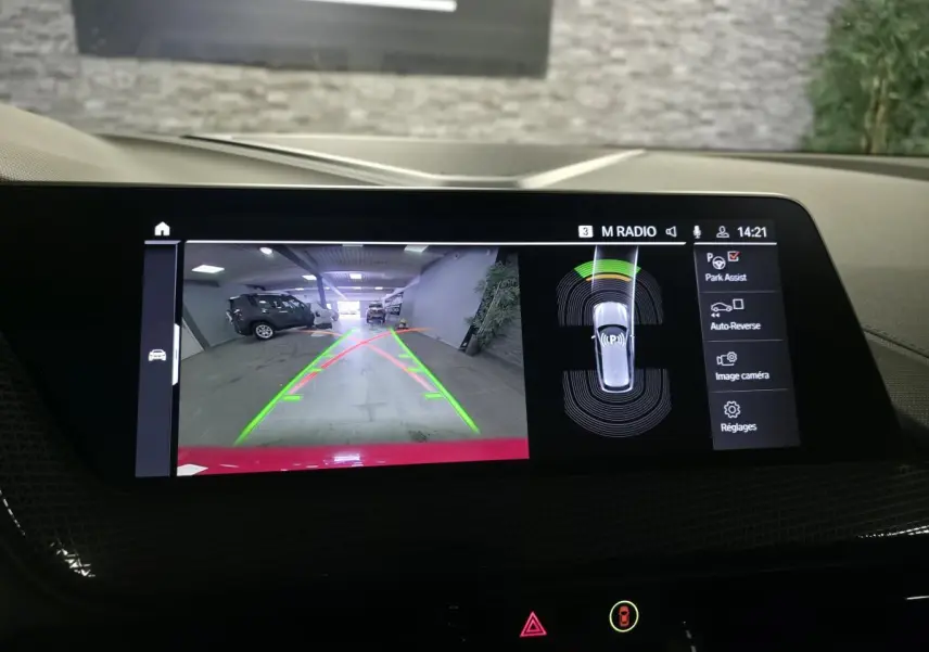 Écran central tactile montrant la caméra de recul d'une BMW Série 1 116d M Sport rouge, vue arrière avec aides au stationnement.