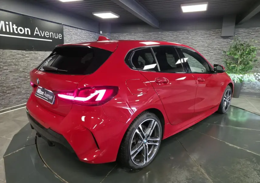 BMW Série 1 116d M Sport rouge vue 3/4 arrière droit en intérieur avec jantes alliage 18 pouces et feux LED.