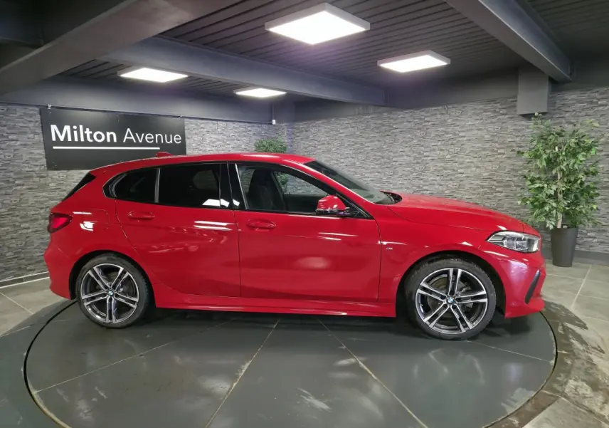 BMW Série 1 116d M Sport rouge vue de profil côté gauche, avec jantes alliage 18 pouces et détails M Sport visibles.