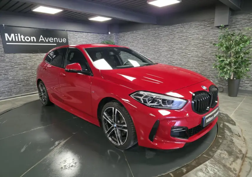 BMW Série 1 116d M Sport rouge vue 3/4 avant droit, calandre noire satinée et jantes alliage 18 pouces bicolores.