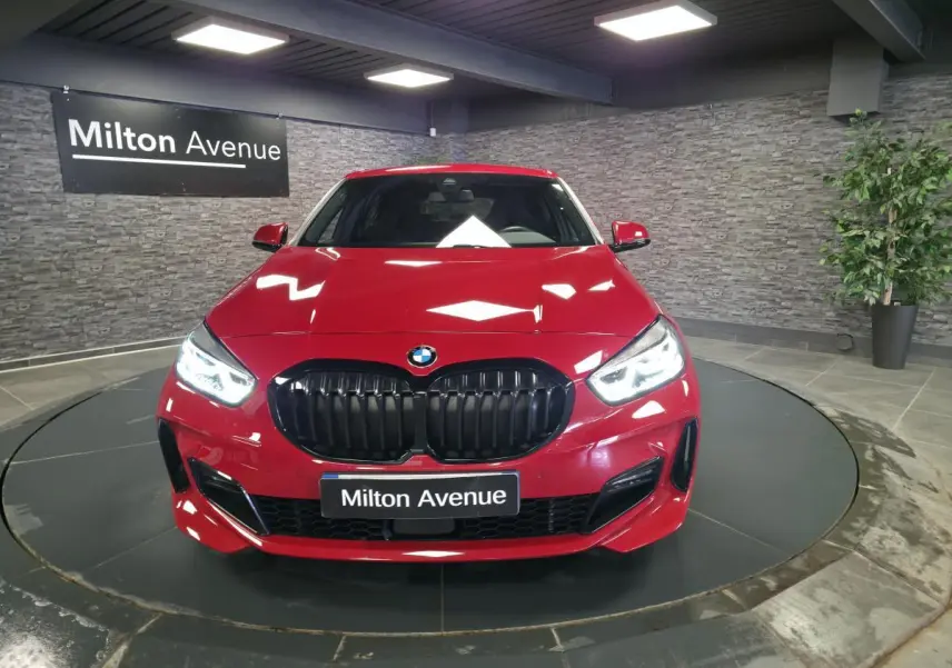 Vue frontale d'une BMW Série 1 116d M Sport rouge métallisé avec calandre noire et phares LED allumés.