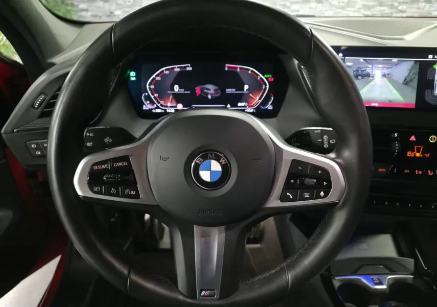 Vue centrée sur le volant M cuir noir de la BMW Série 1 116d 2024, avec tableau de bord numérique et écran de caméra de recul.