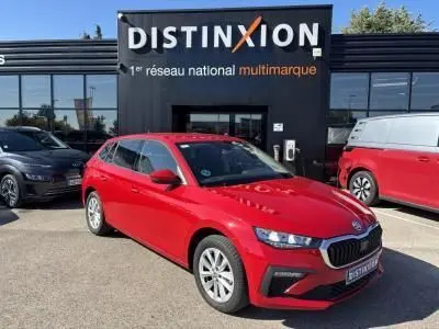 Vue 3/4 avant d'une SKODA SCALA rouge velvet metal garée devant un concessionnaire Distinxion par temps ensoleillé.