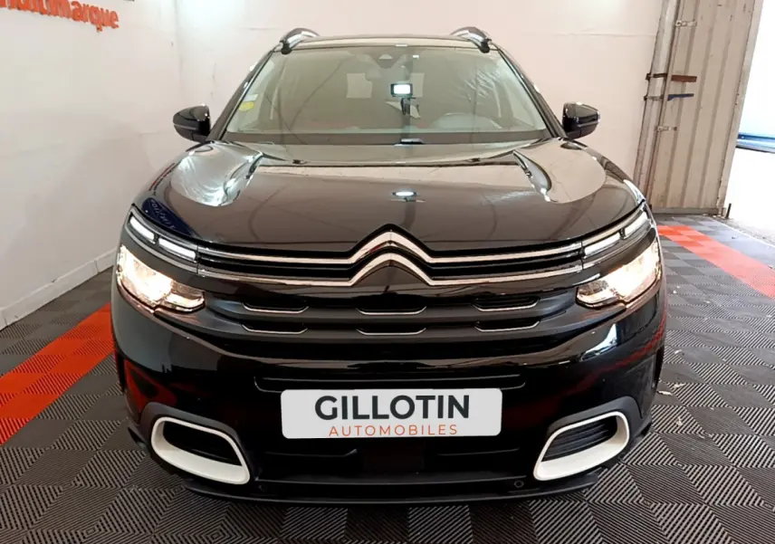Citroën C5 Aircross noir vue de face en intérieur, avec calandre chromée et feux allumés.