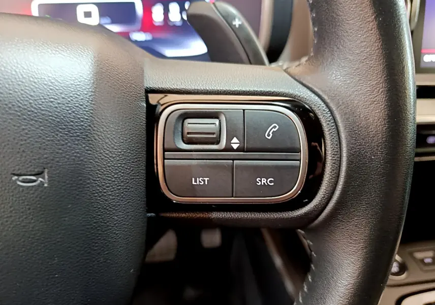 Gros plan sur les commandes gauche du volant cuir du Citroën C5 Aircross noir, avec affichage numérique en arrière-plan.