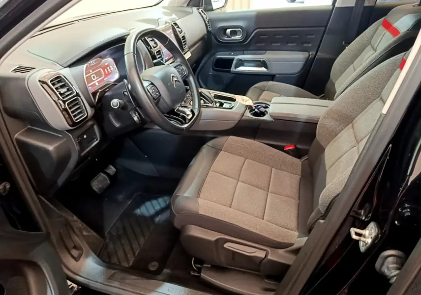 Intérieur côté conducteur du Citroën C5 Aircross noir, montrant le tableau de bord et sièges gris avec accoudoir central.