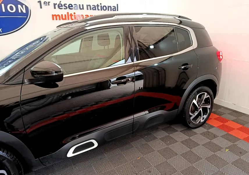 Profil côté gauche du Citroën C5 Aircross noir 2020 avec jantes alliage et barres de toit visibles en intérieur showroom.