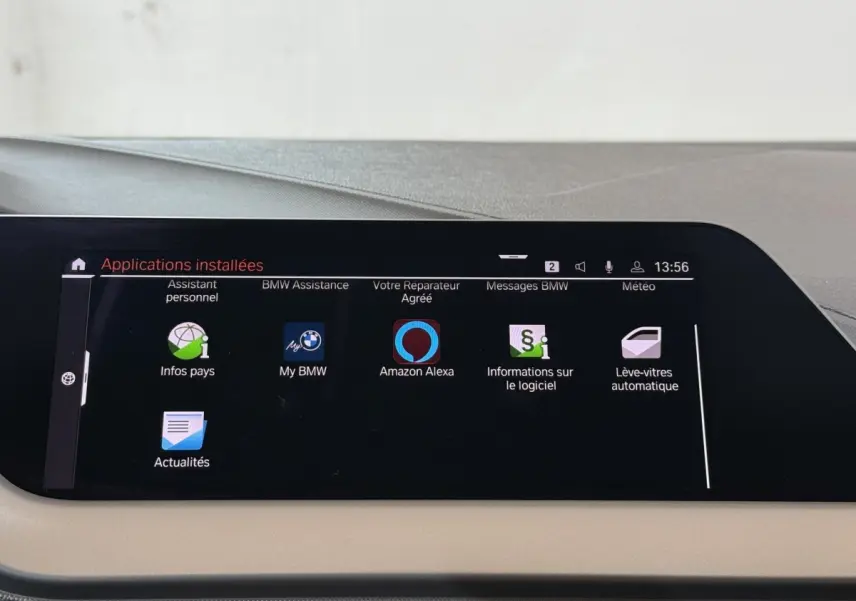 Écran tactile central affichant les applications installées dans le tableau de bord beige d'une BMW Série 1 noire.