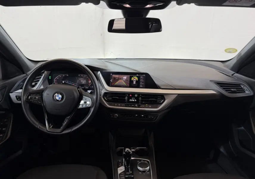 Vue intérieure avant de la BMW Série 1 116d Business Design noire, tableau de bord moderne avec écran tactile et volant cuir multifonctions.