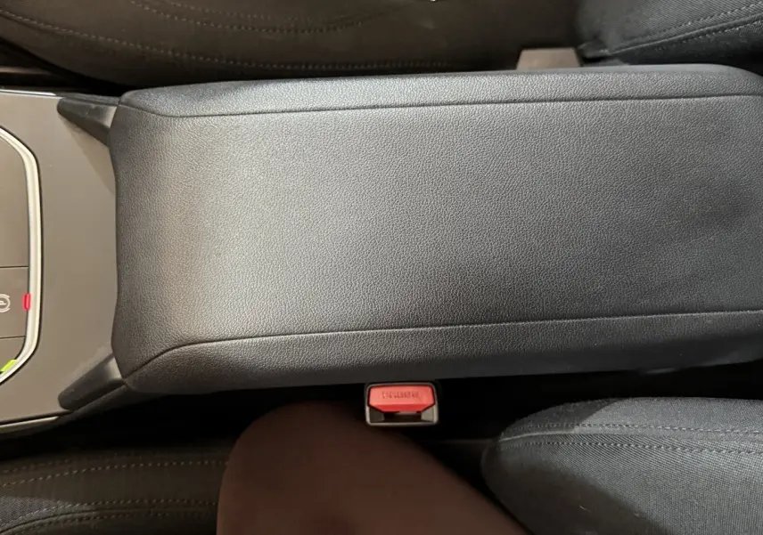 Vue rapprochée du couvercle de la console centrale noire et du bouton de ceinture rouge dans une BMW Série 1 116d DKG7 Business Design.