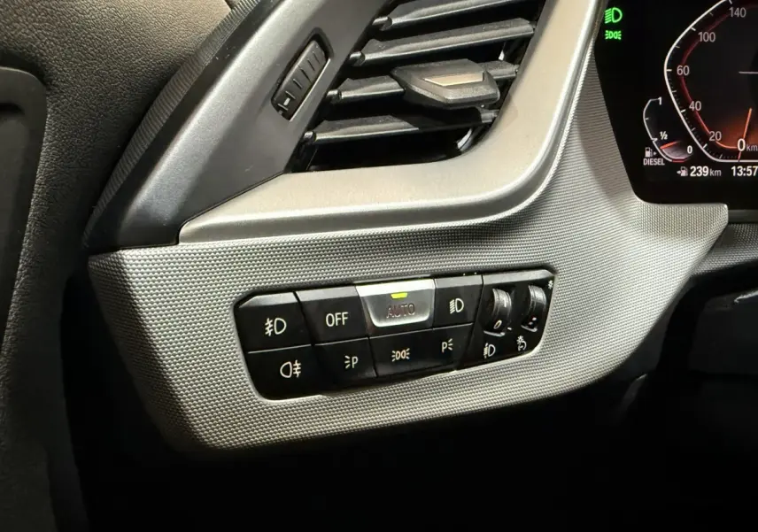 Gros plan sur le tableau de bord gris clair côté gauche de la BMW Série 1 116d, avec commandes d’éclairage et ventilation.