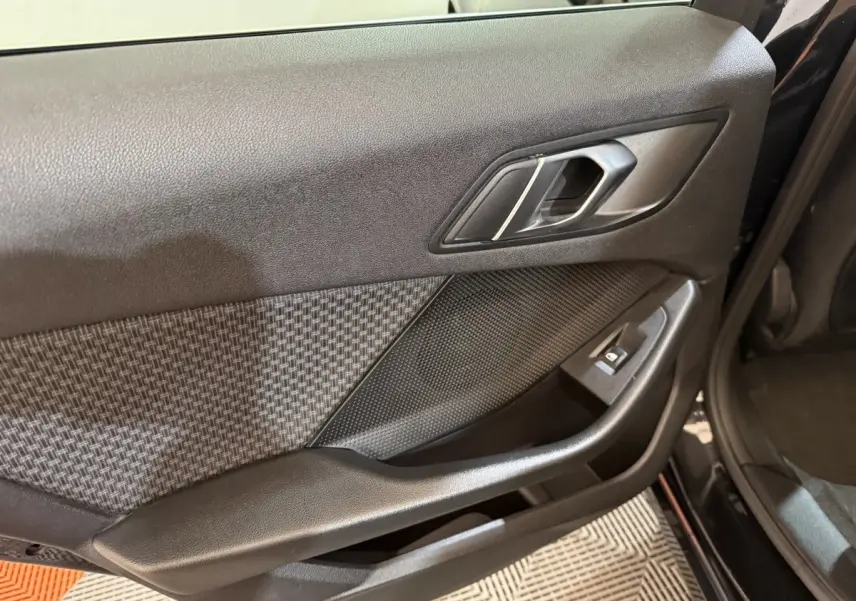 Vue intérieure côté gauche de la porte noire de la BMW Série 1 116d avec insert tissu à motif et commande de vitre.