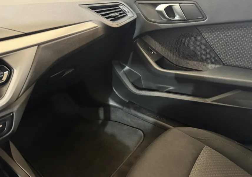 Vue intérieure côté passager avant de la BMW Série 1 116d noire, montrant la portière et le tableau de bord.