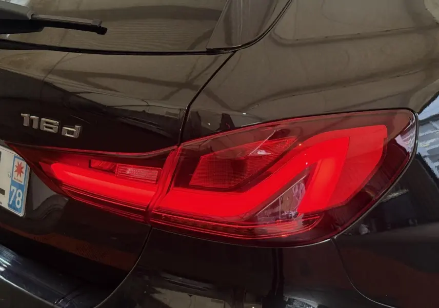 Gros plan sur le feu arrière droit rouge vif d’une BMW Série 1 116d noire, avec logo 116d visible sur le coffre.