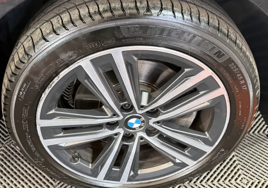 Gros plan sur la roue avant droite d’une BMW Série 1 noire, jante alliage à design étoilé et pneu Michelin.